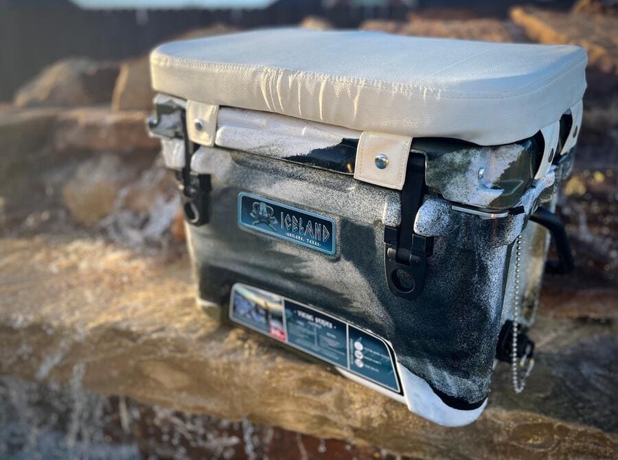 Iceland Cooler with camo finish and white padded seat cushion, designed for comfort and sunlight reflection during outdoor use.