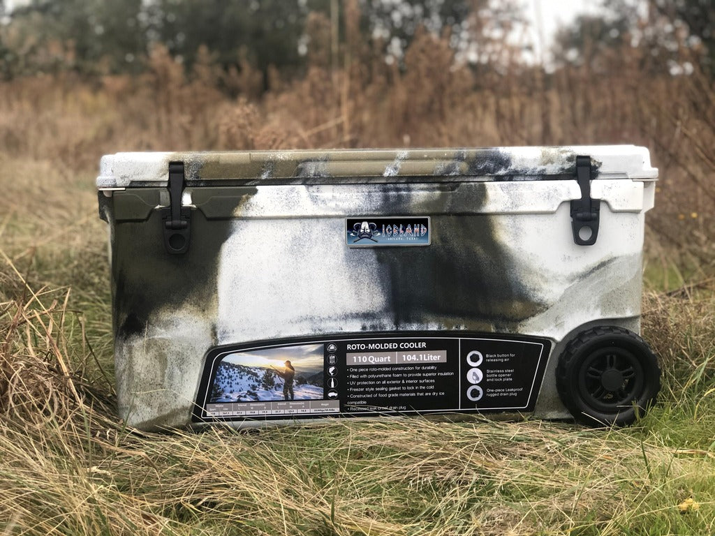 Iceland Coolers Longship Series 110-quart roto-molded wheeled cooler in camo design, shown outdoors in a grassy field.
