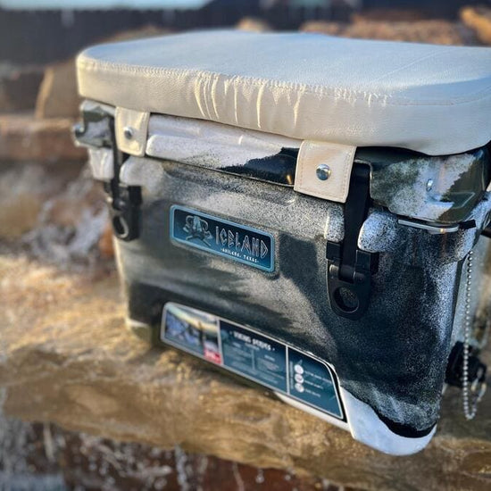 Iceland Cooler with camo finish and white padded seat cushion, designed for comfort and sunlight reflection during outdoor use.