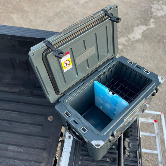 Open gray Iceland Cooler with Glacier Ice Pack and basket inside, shown on a truck bed ready for outdoor use.