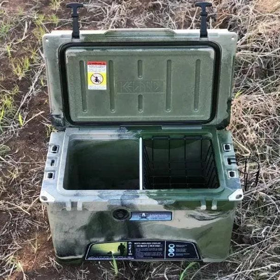 Open green camo Iceland Cooler outdoors, featuring a center divider and black hanging basket for dry storage during hunting or camping.