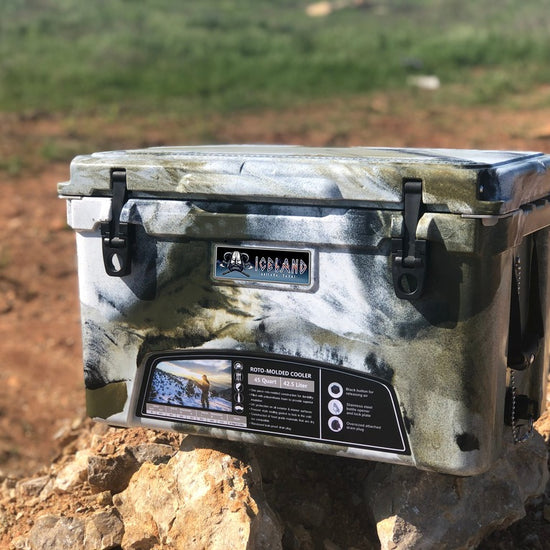 Camo-pattern Iceland Coolers Viking Series 45QT hard cooler placed on rocks in a rugged outdoor setting.