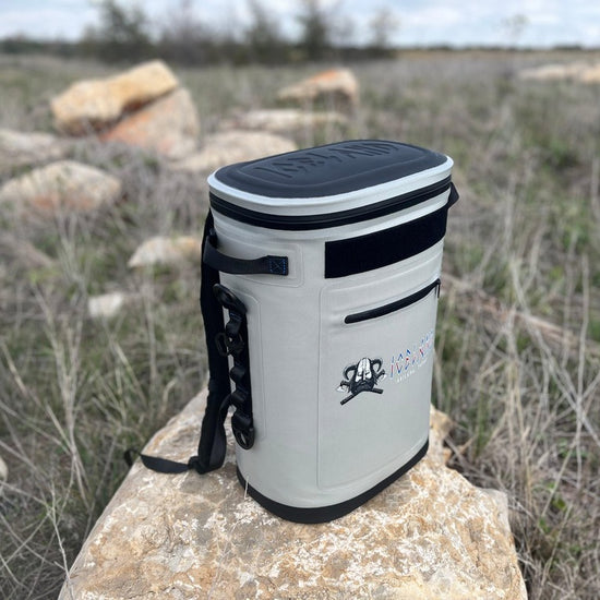 Gray 30-can soft cooler with black accents and shoulder strap, sitting on a rock in a grassy field.