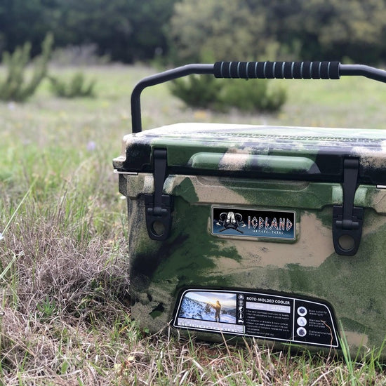 Camouflage Iceland Coolers Viking Series 20QT hard cooler with carry handle, shown outdoors in a grassy field.