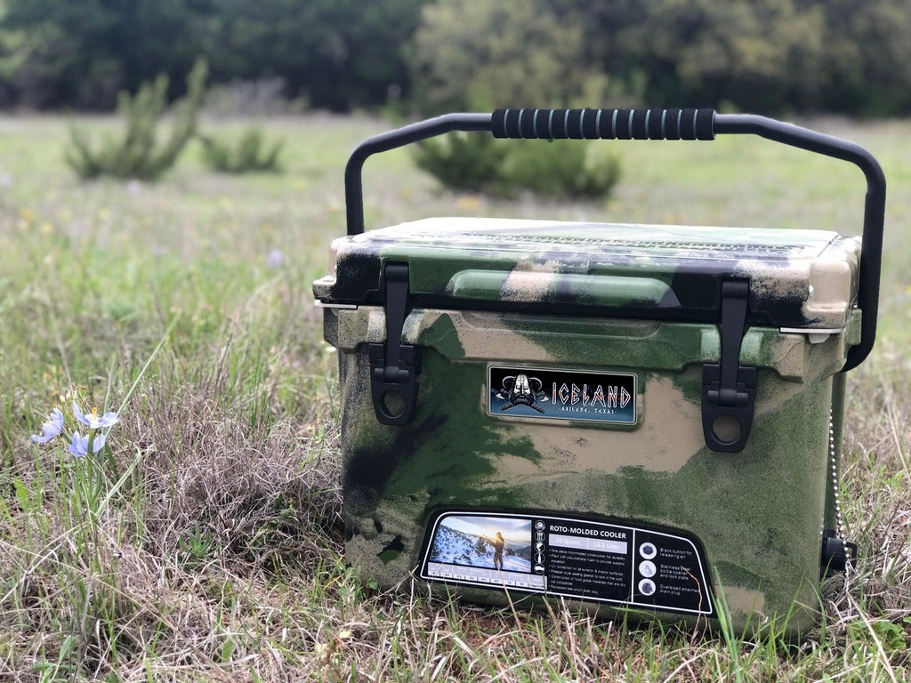 Camouflage Iceland Coolers Viking Series 20QT hard cooler with carry handle, shown outdoors in a grassy field.