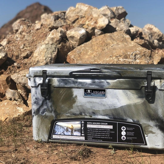 Iceland Coolers Viking Series 75 QT in arctic camo, shown outdoors on rocky terrain with dual-latch front and product label visible.