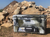Iceland Coolers Viking Series 75 QT in arctic camo, shown outdoors on rocky terrain with dual-latch front and product label visible.